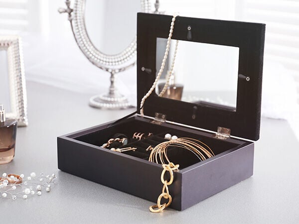Grey rectangular jewelry box sits open on a lighter gray surface to reveal gold and pearl jewelry inside, nested on a black interior.