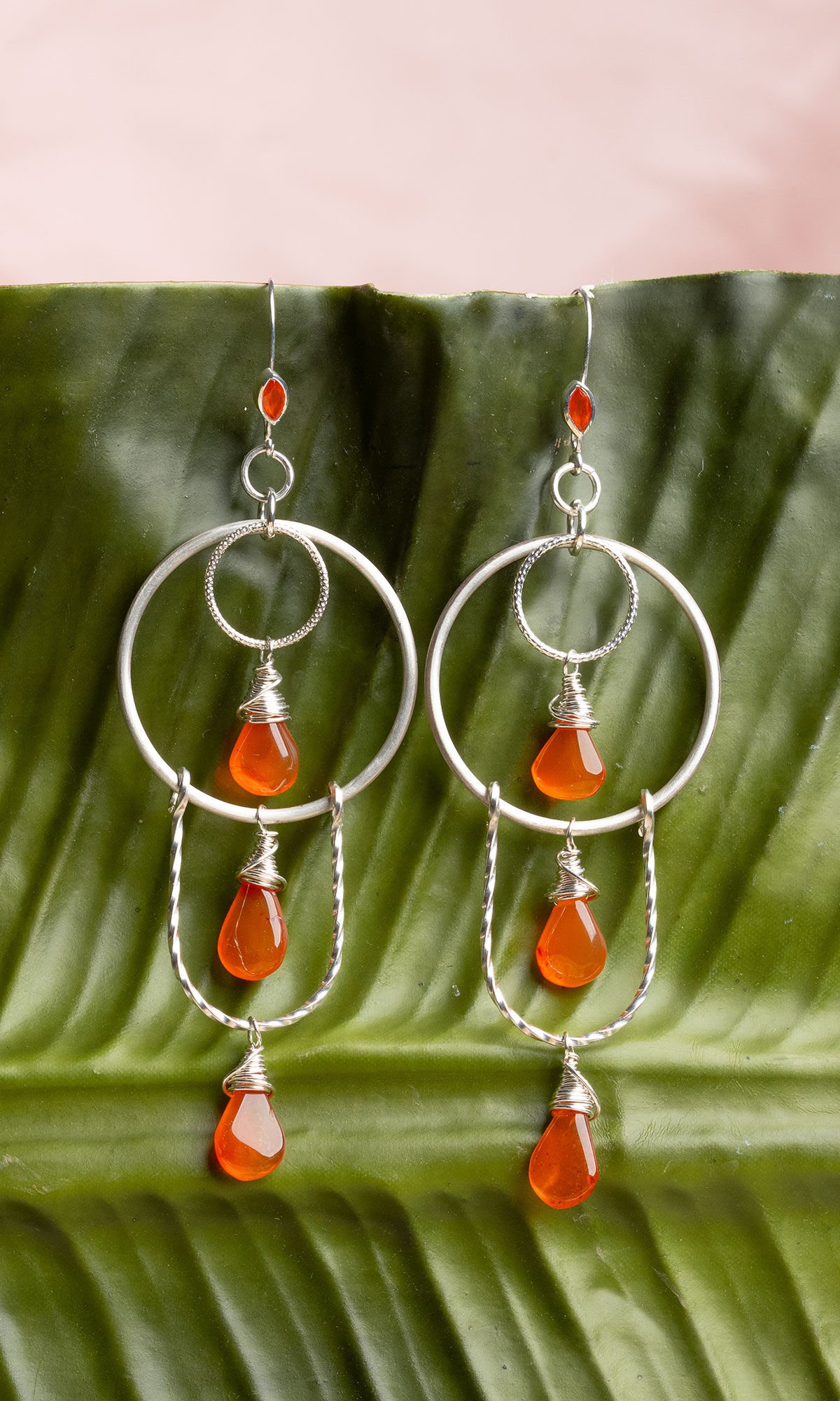 orange and silver earrings hanging from banana leaf