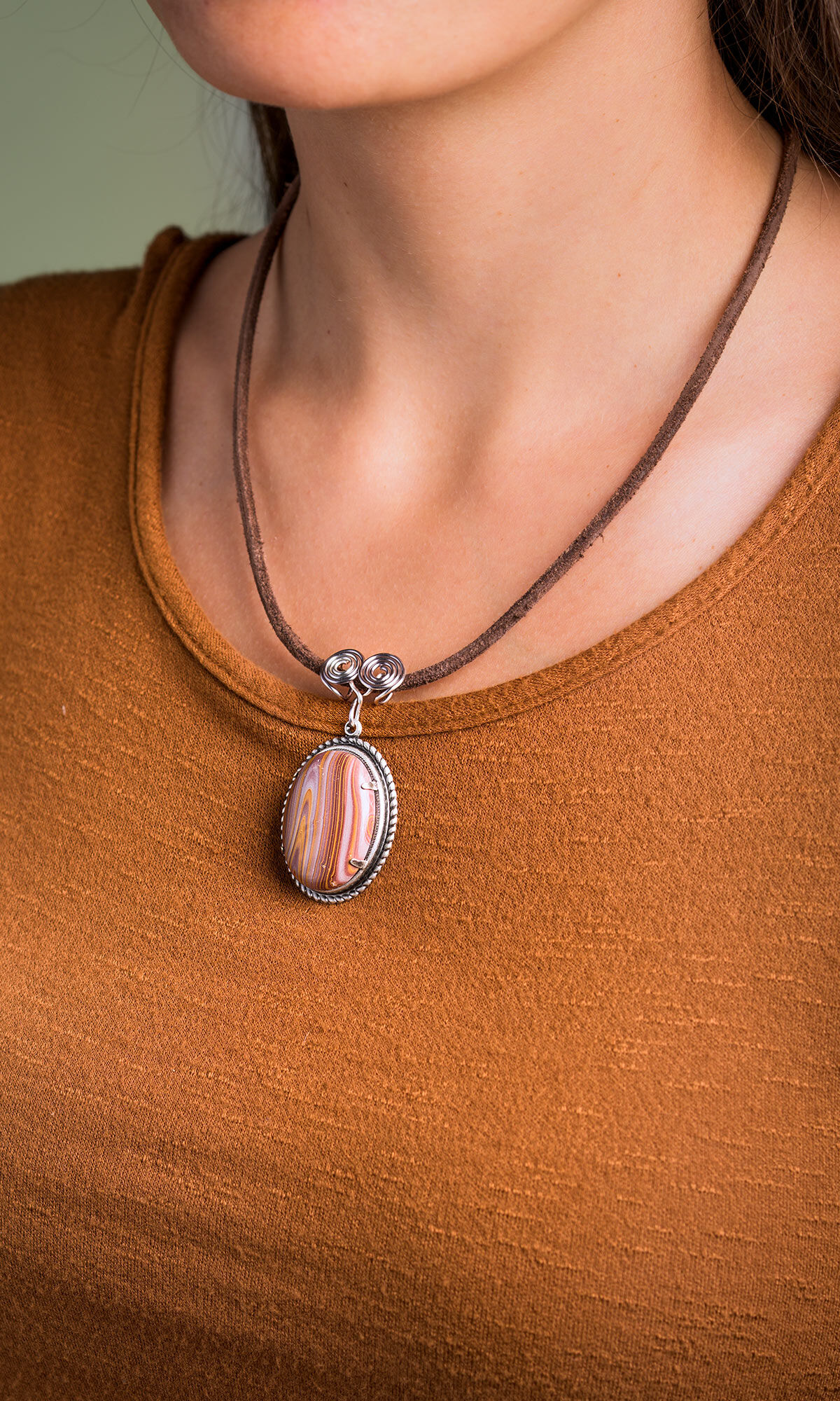 Close up shot of model's neck wearing Design Idea R F 4 D with Leather Cord and Natural Autumn Hickoryite Oval Cabochon with a green background