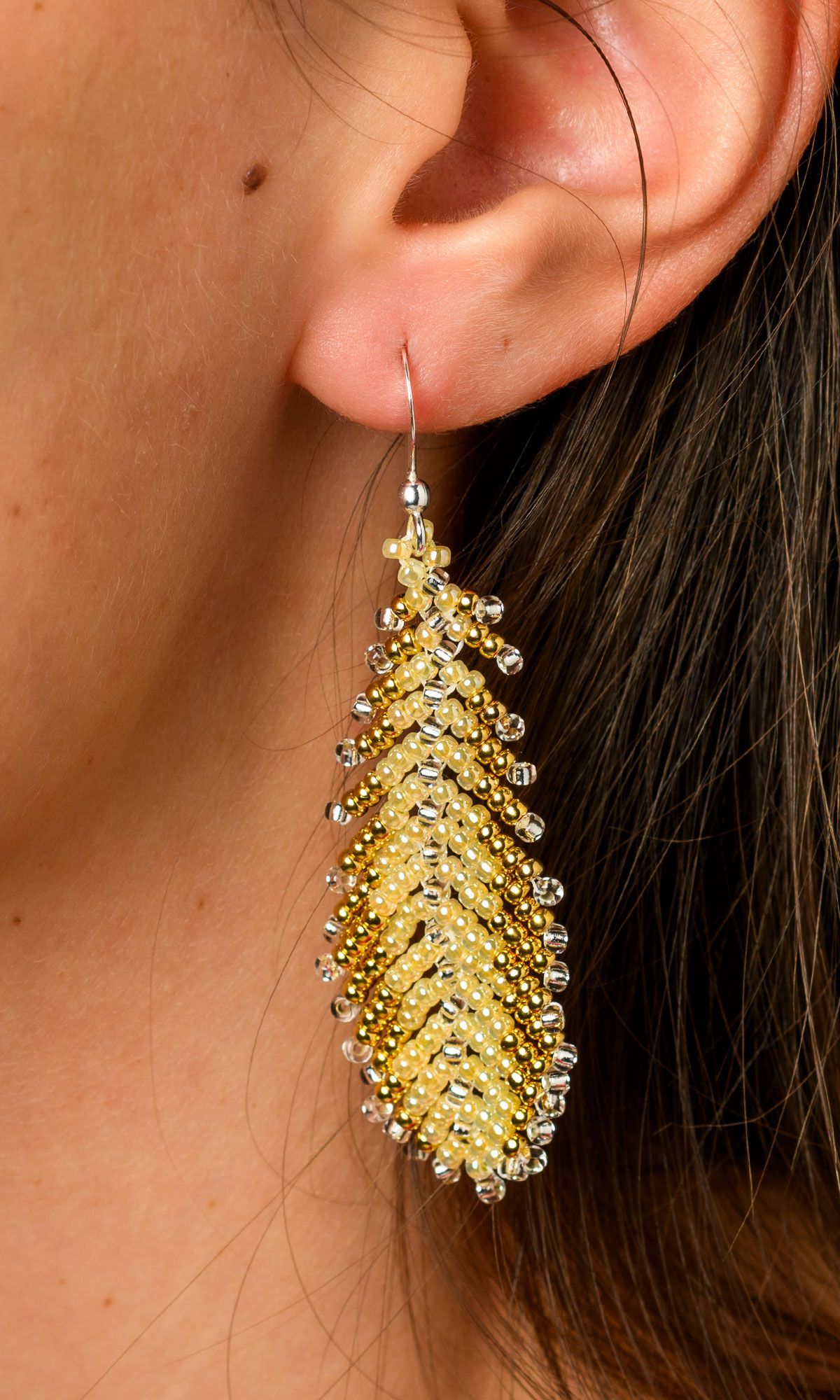 Closeup of a ear wearing Design Idea S B 3 3 &ndash; Seed beaded earrings look like feathers with pale yellow seed beads in the center and gold seed beads on the edges.
