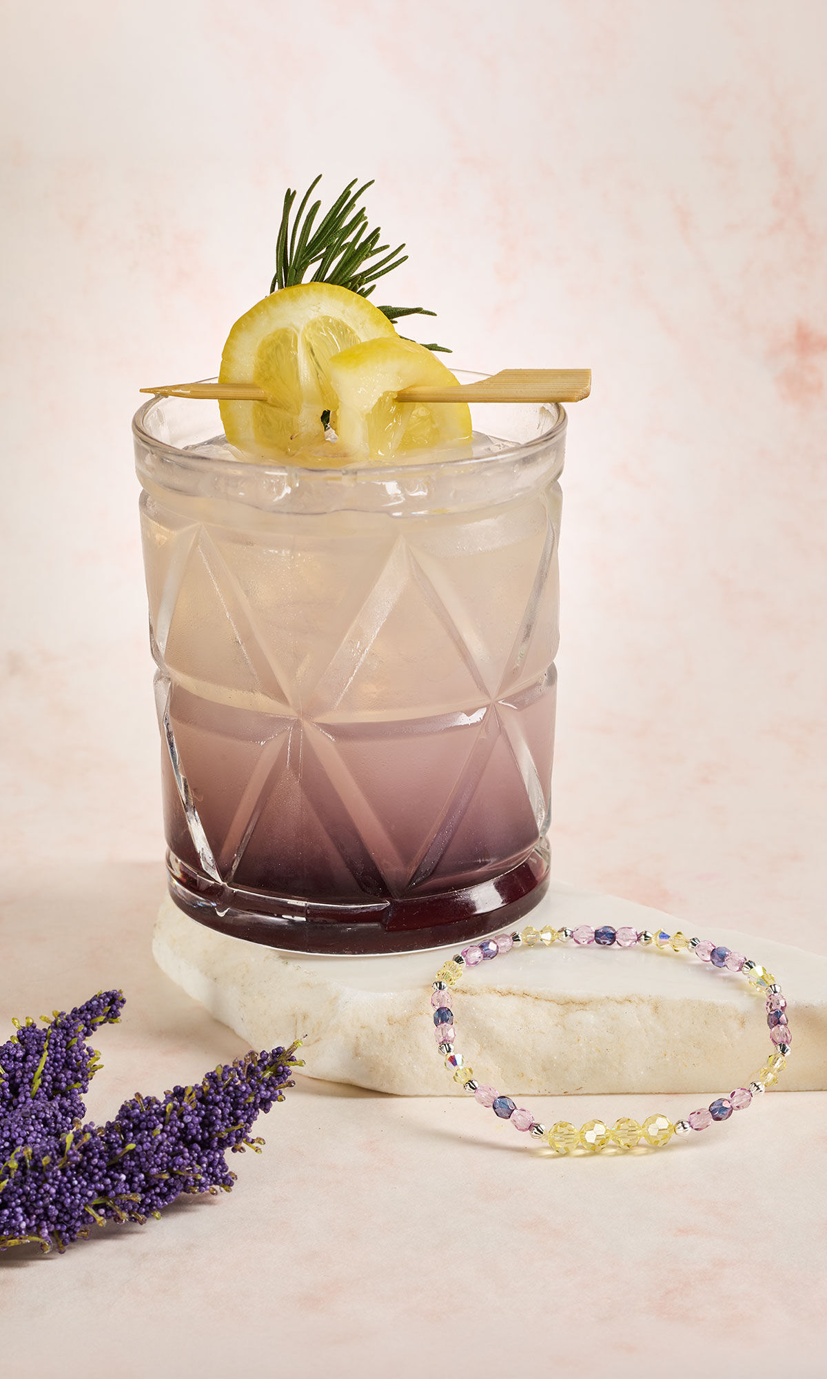 glass with lavender ombre liquid and lemon toothpick garnish with a purple and clear bracelet nearby