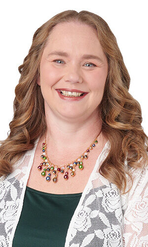 Design Idea Q F 2 6 - Woman wearing a white lace cardigan and a vibrant, multi-colored beaded cluster statement necklace.