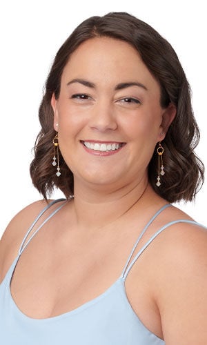 Woman wearing delicate, gold-toned drop earrings with clear, faceted crystal beads hanging in parallel vertical strands.