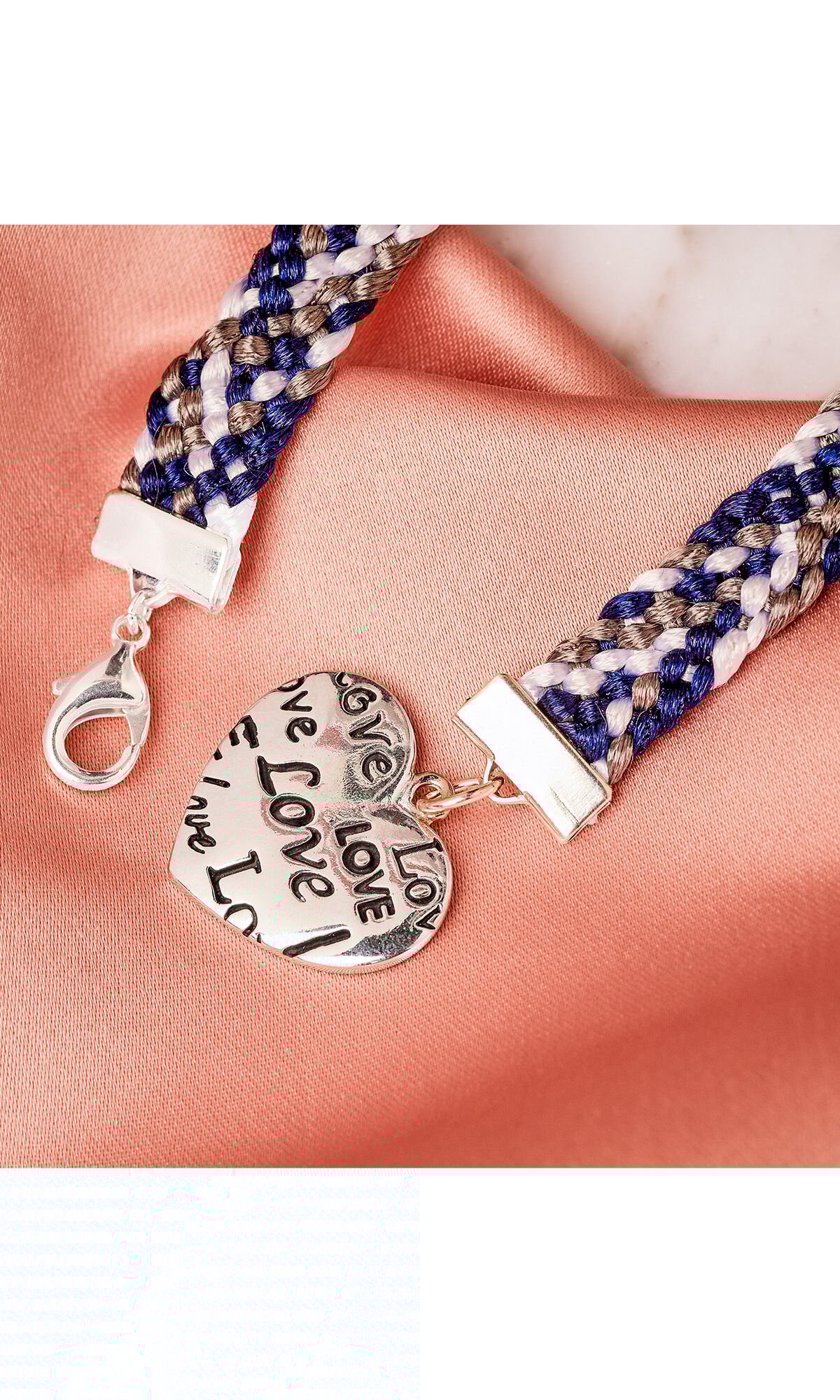 Design Idea R C 3 K 10-Strand flat braided bracelet with white, silver, and blue cord on peach satin fabric showing clasp and heart charm