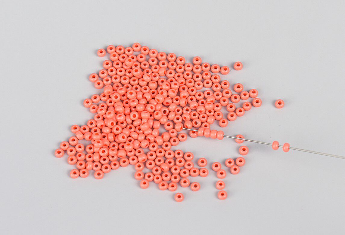 Stringing orange seed beads onto a needle