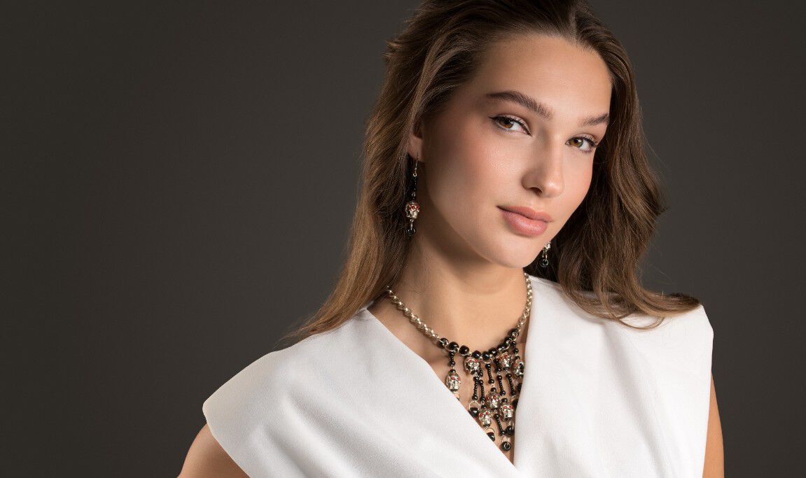 Silver chain necklace with seven pendants, each with a red-eyed skull bead and black seed beads configured to look like bones.