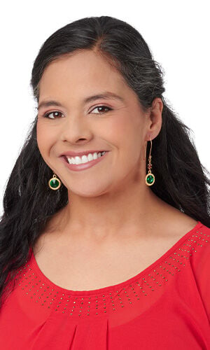 Close-up of a smiling person wearing gold drop earrings featuring vibrant, round green gemstones