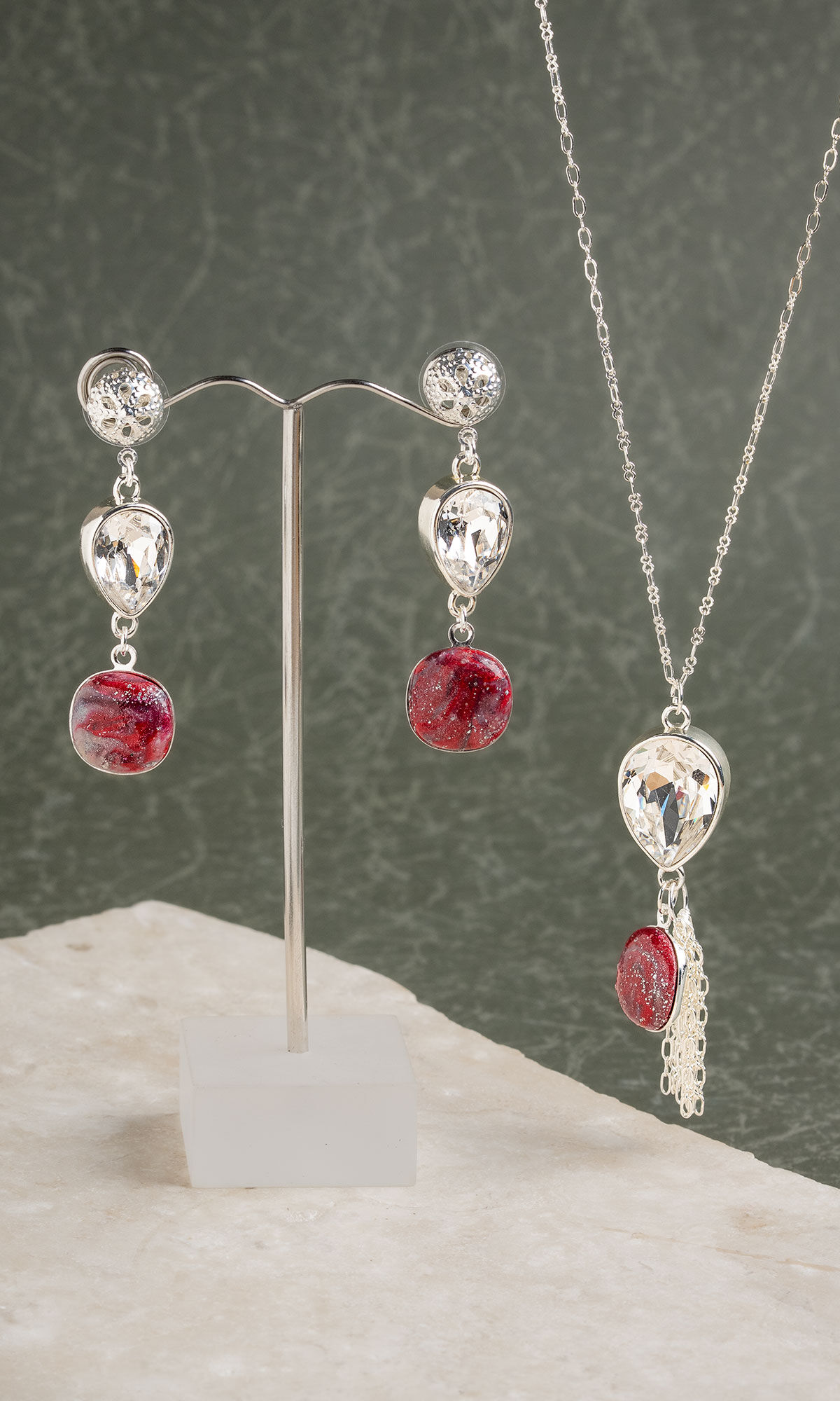 Earrings hanging from silver wire tree with necklace beside them.