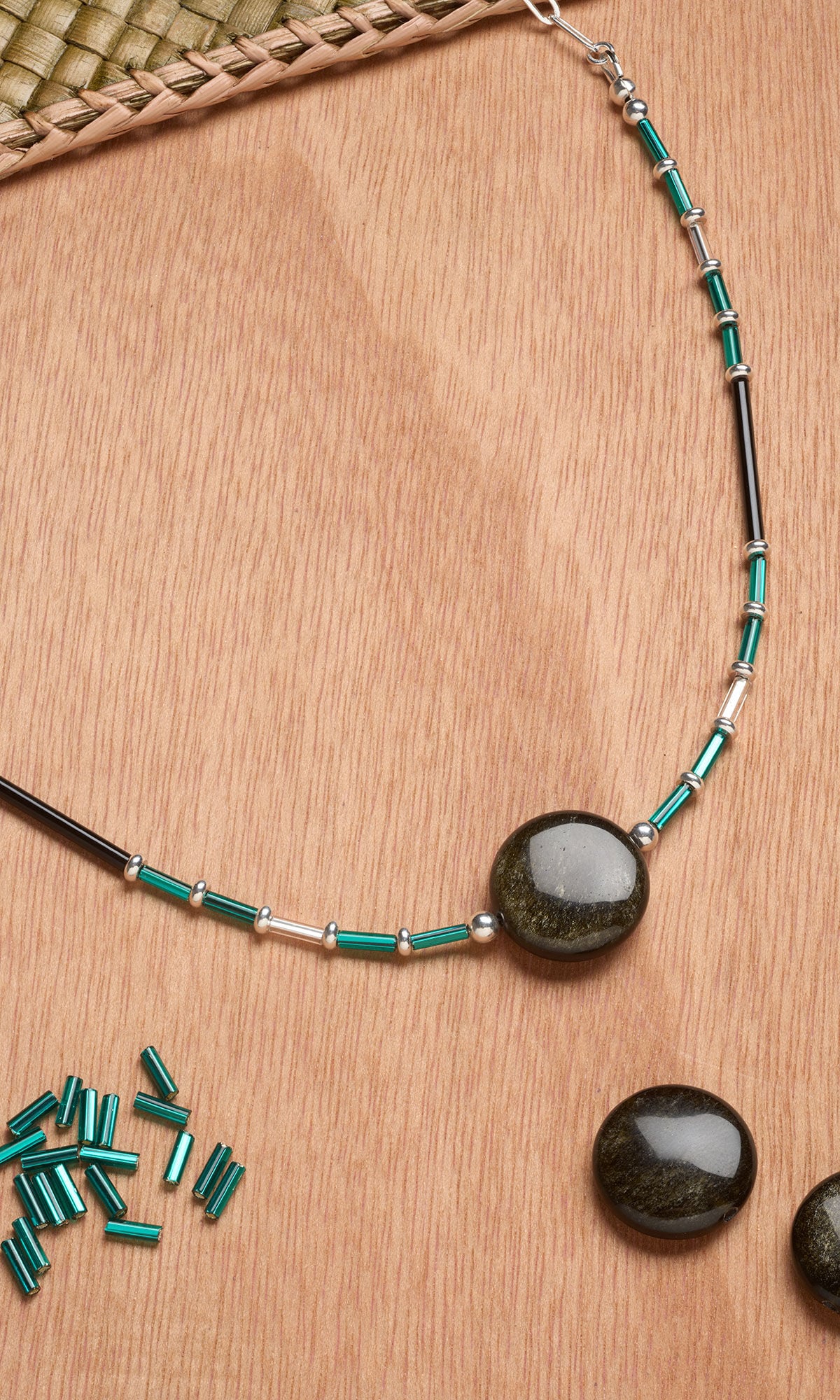 Beaded necklace with dark stone pendant and green metal bugle beads on wooden surface