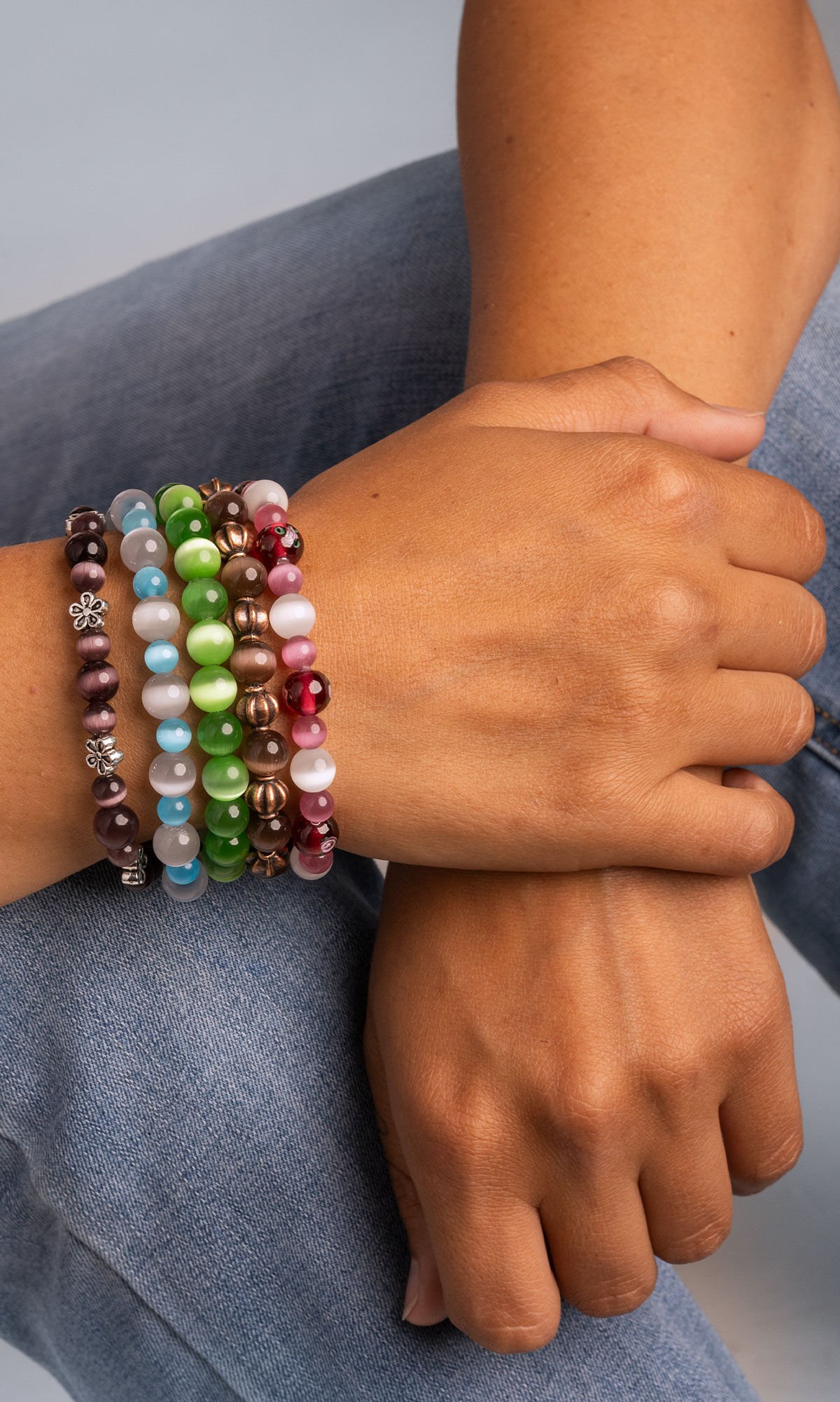 Photo of hand crossing wearing five beaded stretch bracelets shimmering in shades of green, blue, purple, pink and brown.