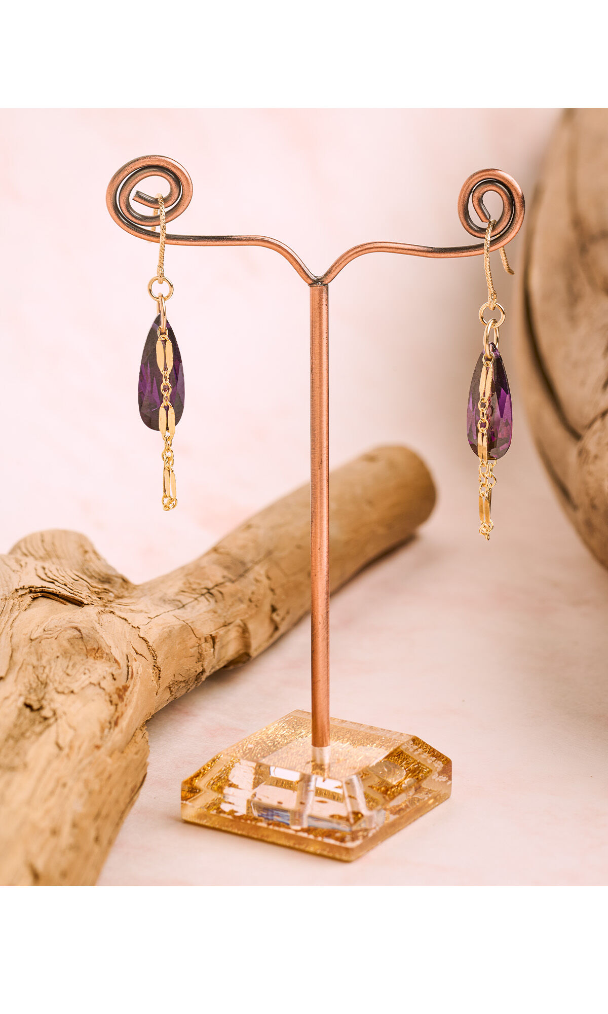 Design Idea R C 3 8 earrings hanging on a display with pink background and driftwood lying next to it