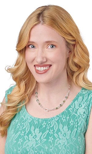 A woman wears a detailed silver link chain necklace decorated with small, dark square beads.