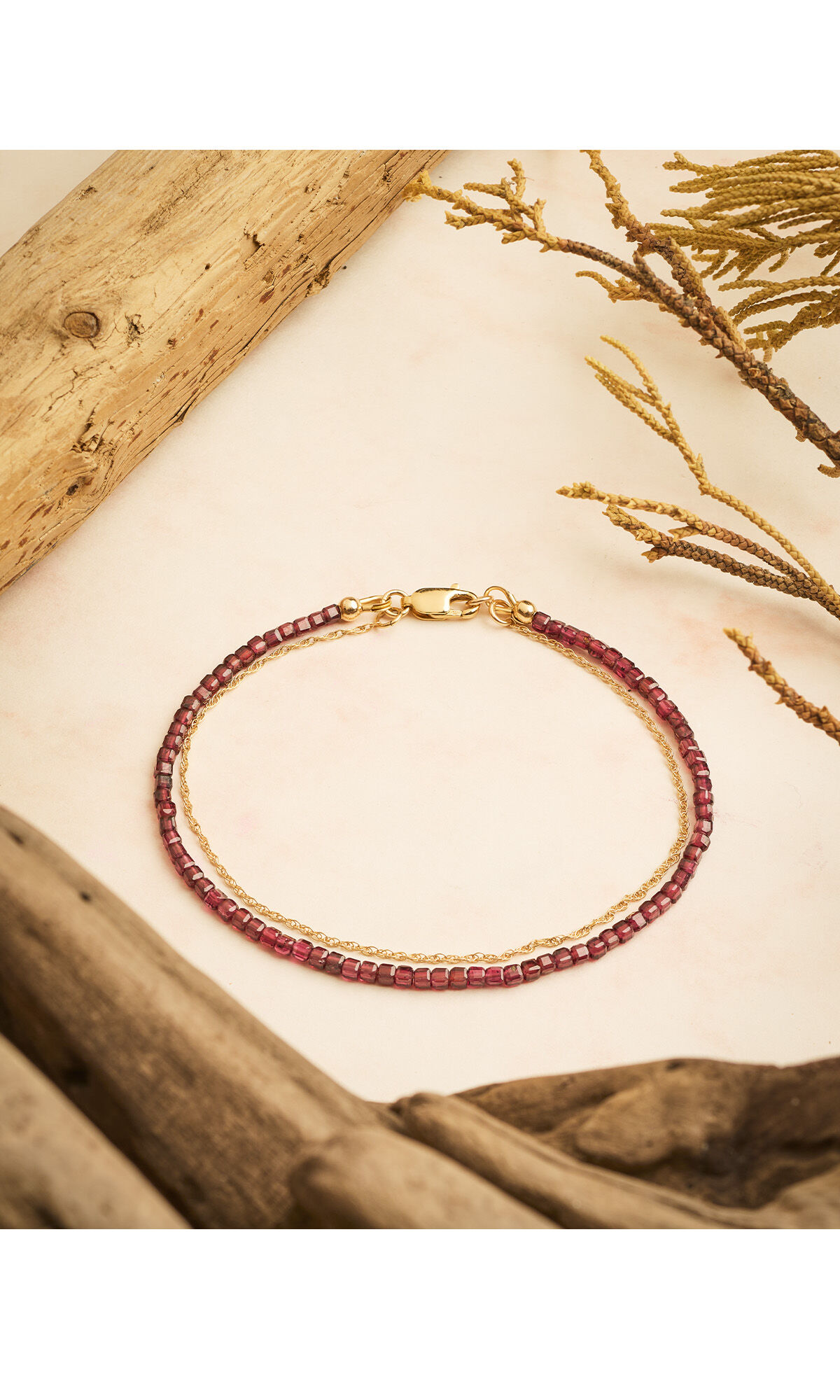 Design Idea R F 4 8 bracelet hanging over a cream-colored background next to gnarled wood 