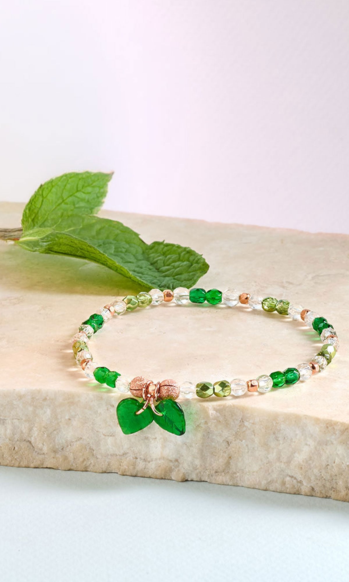 Green Clear and Copper bracelet placed on a piece of beige granite with a mint leaf in the background