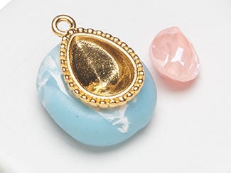 Empty teardrop setting sitting on blue clay with pink stone next to it