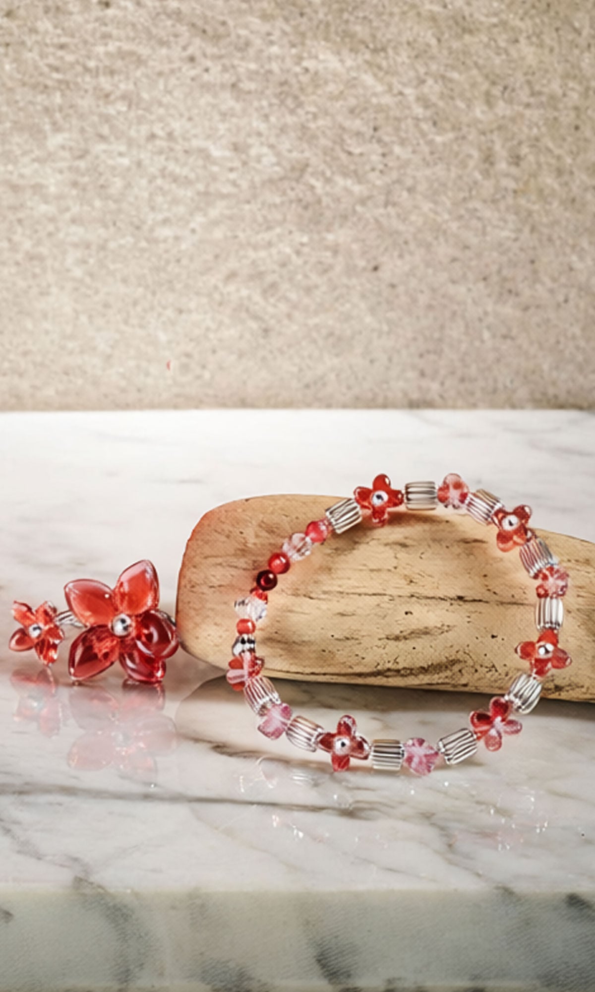 Pink, Red and clear bracelet place on a piece of wood on a slab of gray and white marble with some glass decorative flower next to the bracelet