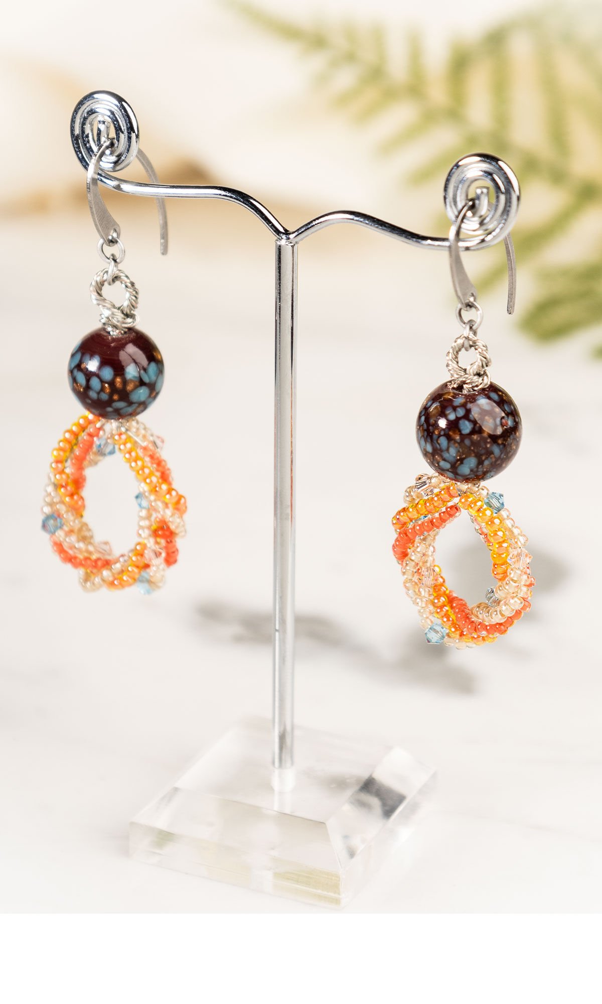 Design Idea R D 2 M Single-Strand Necklace and Earring Set with Preciosa Seed Beads and Crystal Passions&reg; Bicones on a clear earring stand with a subtle fern in the background