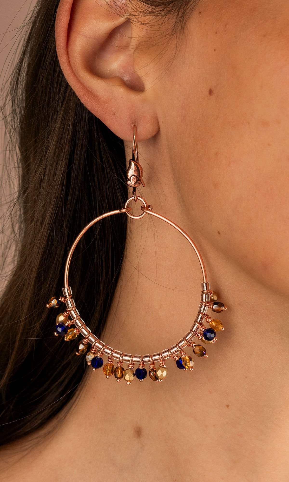 Close up of design idea R H 2 8 Earrings with large circles of wire, and each circle has 24 small beaded drops in a pattern of blue and gold hues.