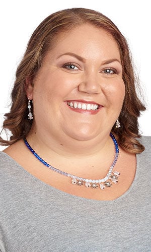 Woman wearing a Christmas themed beaded necklace with silvery charms and matching drop earrings.