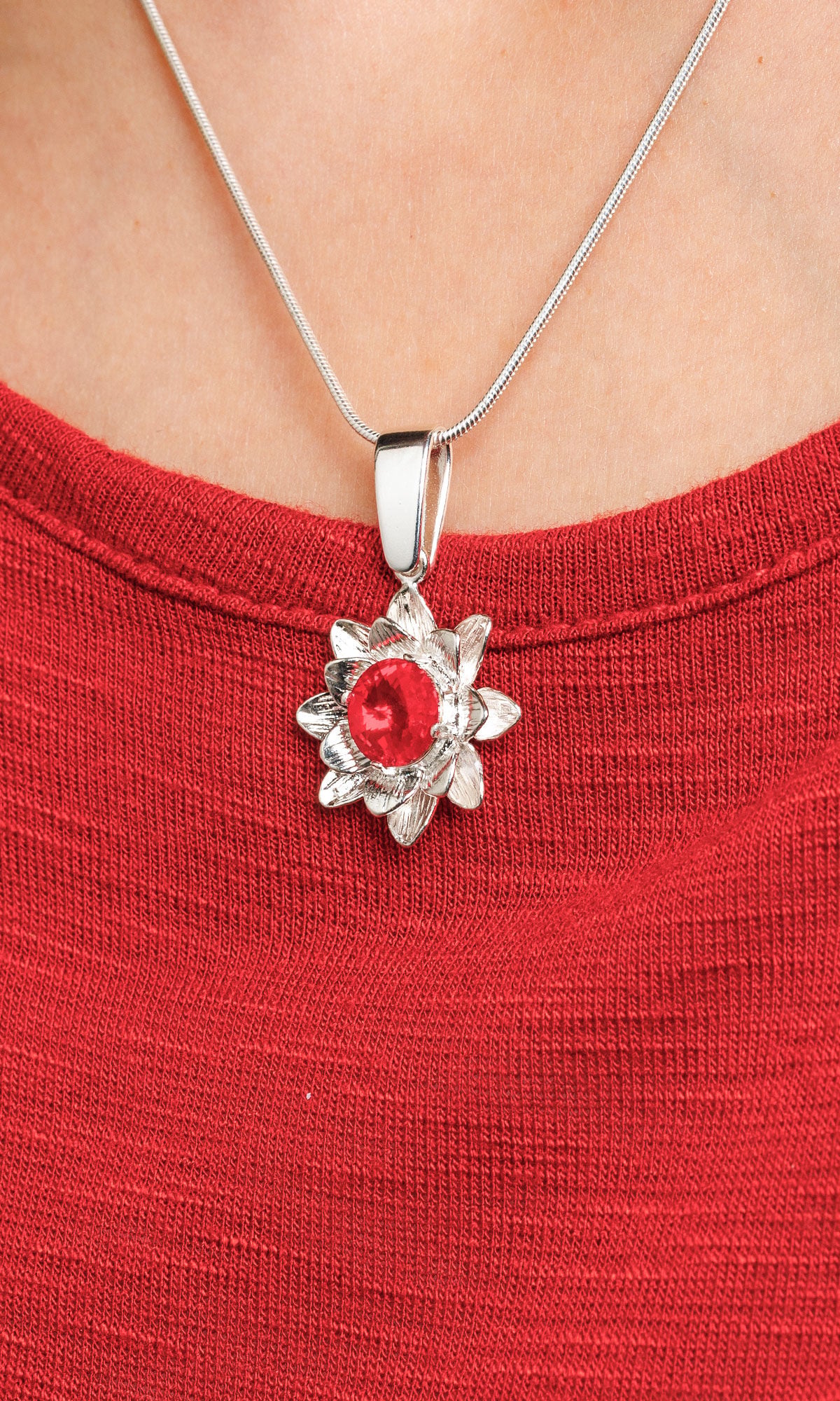 Closeup of a silver flower pendant necklace with a red gemstone center on a silver chain