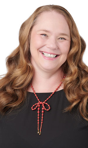 A woman wearing a unique bow-shaped necklace crafted from vibrant red seed beads in contrasting sizes.