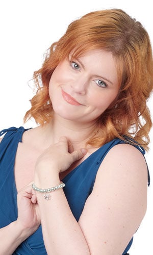 A women highlights a mint-green faux pearl strand bracelet accented by a single shimmering metallic snowflake charm that dangles loosely from the center.