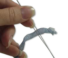 A hand holding an open needle with stringing material inside.