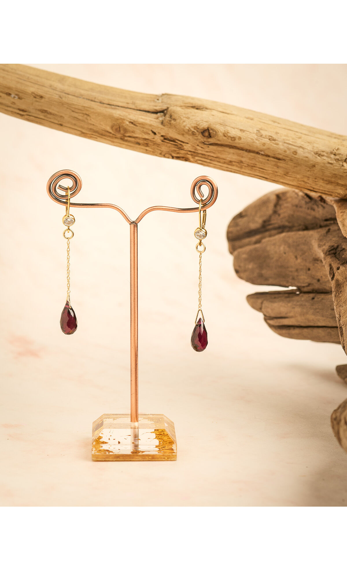 Design Idea R F 4 8 earrings hanging over a cream-colored background next to gnarled wood 