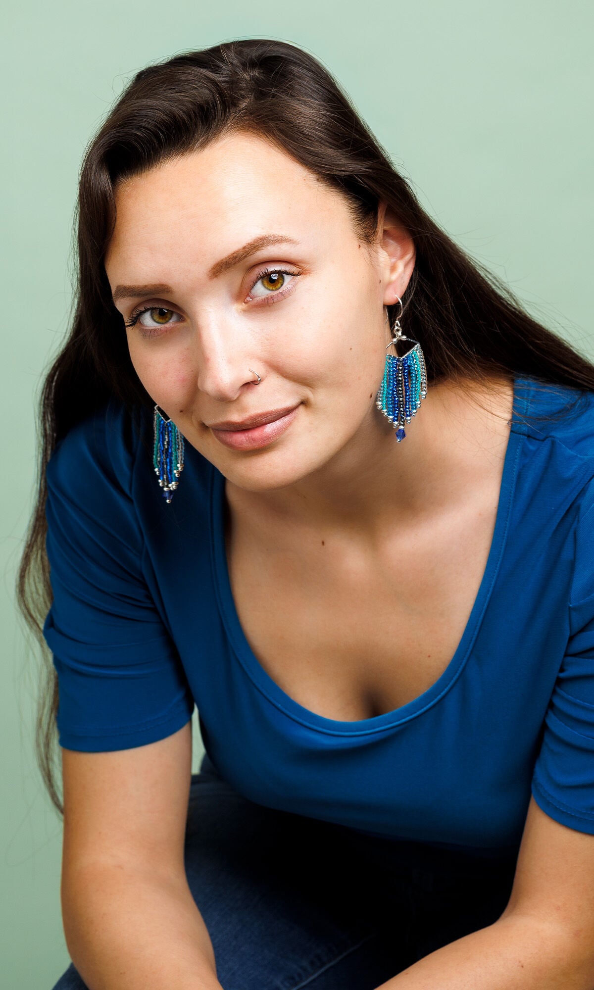 Model in a blue shirt wearing Design Idea S B 2 X &ndash; Each earring has a silver diamond wider than it is tall with nine columns of seed beads hanging from it in various shades of blue.