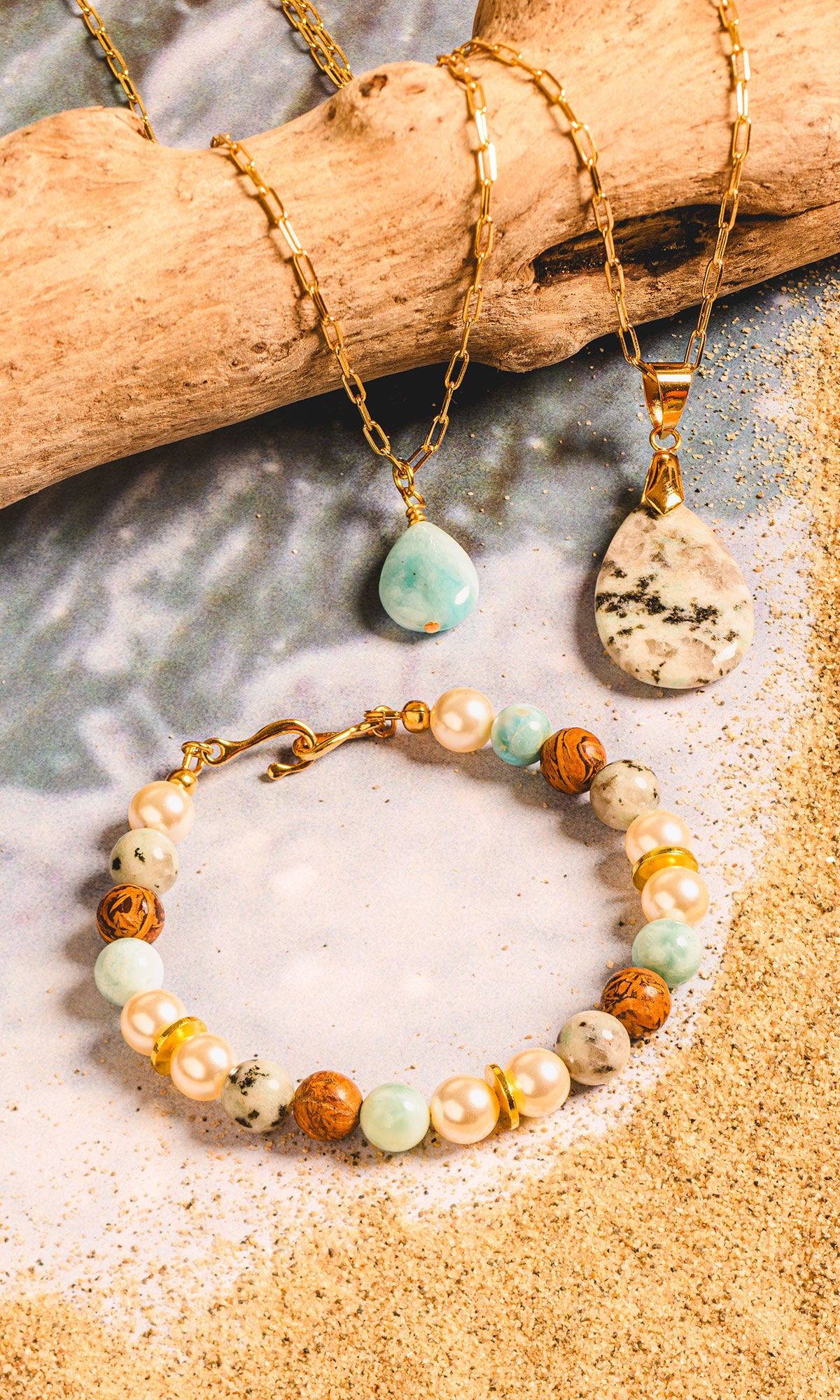 This beach-inspired jewelry collection features two gold paperclip chain necklaces&mdash;one adorned with a teardrop light-blue larimar pendant and the other with a larger speckled jasper stone. It also includes a coordinating beaded bracelet made from alternating creamy pearls, sky-blue larimar spheres, and earthy brown jasper beads.