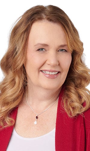 A woman wearing a red jacket and a silver-toned chain featuring a two-tiered dropdown pendant with flower-shaped charm.