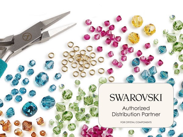 Scattered blue, brown, magenta and yellow crystal beads with a pile of golden jump rings near the center of the image. Pliers with blue handles are on the left and a text box with the words "Swarovski Authorized Distribution Partner for crystal components" on the lower right.