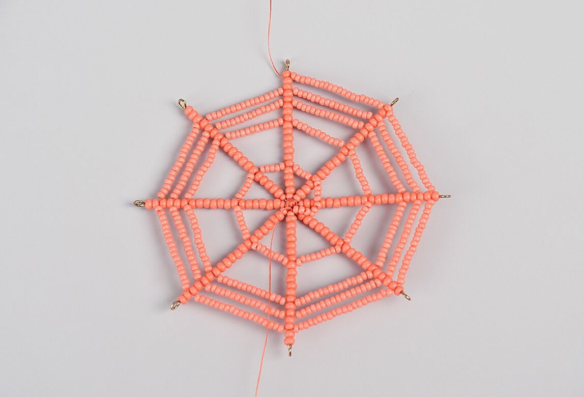 Orange seeded beaded thread is strung in a spiral onto the ornament frame.