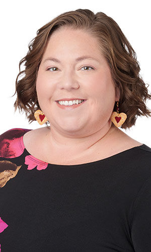 A woman showcasing a pair of polymer clay earrings that are hearts and look like jelly filled cookies