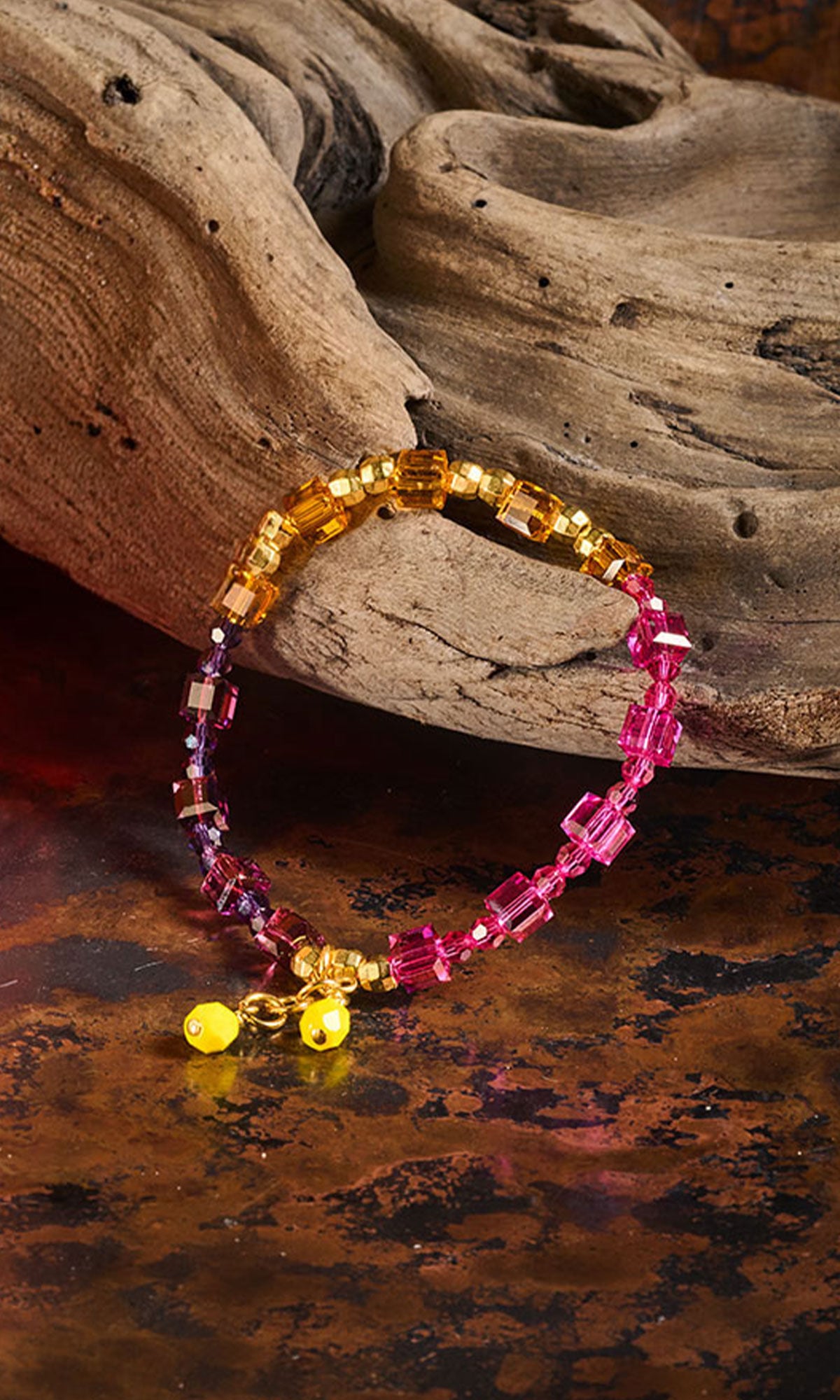 Pink and Yellow bracelet placed on a piece of driftwood on a copper metal sheet