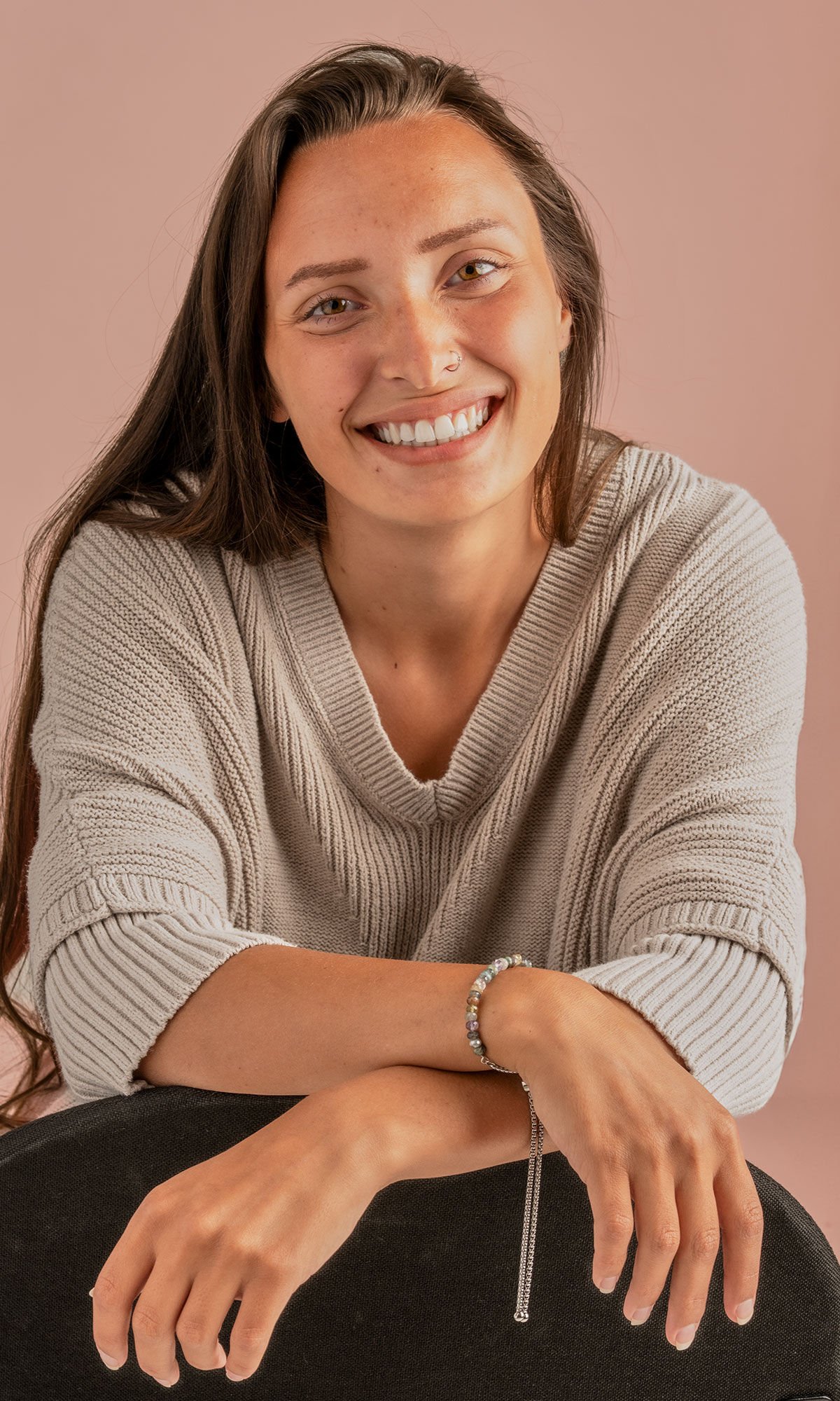 model wearing a tan 3/4 sleeve top wearing design idea R G 2 Y bracelet. Half of the bracelet is subdued shades of multi-colored gemstone beads. The other half is a thick chain that ends in two steel balls and has a large slider bead to adjust size.