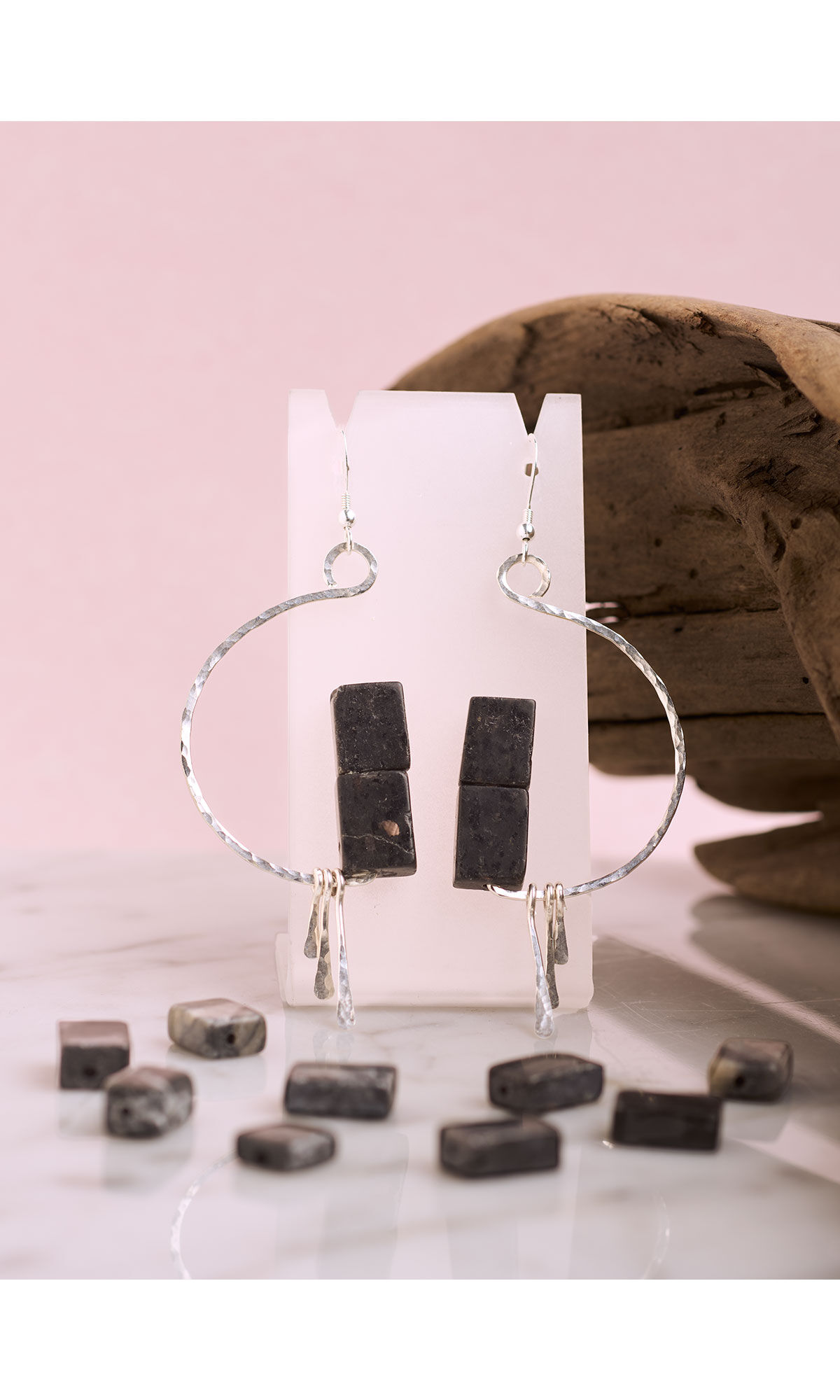Design Idea R G 2 U - Hammered silver earrings shaped like a half circle with three smaller hammered wires dangling from the bottom and two dark rectangular beads sitting atop the bottom of the curve displayed amid scattered hypersthene rectangle beads with a rock in the background