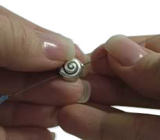 A hand is holding a metal bead with a needle.