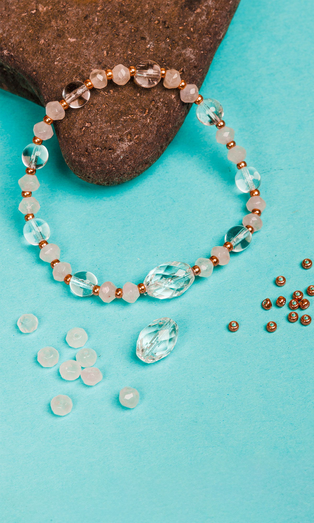 Design Idea S D 3 K &ndash; Stretch bracelet made with rose quartz and quartz crystal gemstone beads and Miyuki seed beads resting on a rock against a blue background