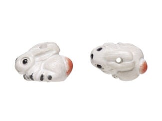 White ceramic rabbit bead. The rabbit has black toes and eye and a brown tail and is facing to the left.