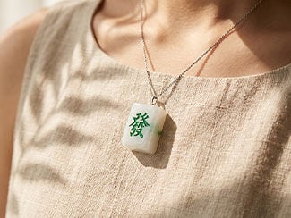 Woman in a linen dress wearing a rectangular white mahjong tile pendant with a green symbol on a delicate chain.