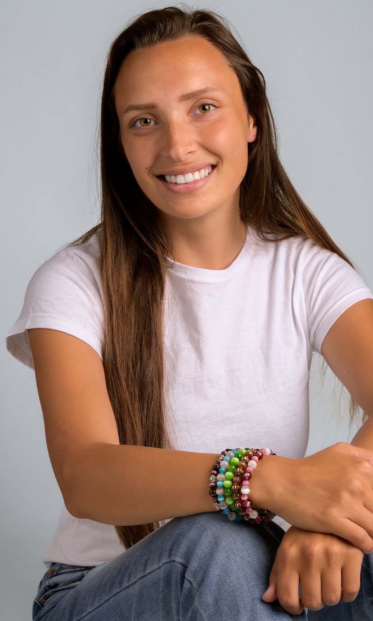Model sitting wearing five beaded stretch bracelets shimmering in shades of green, blue, purple, pink and brown.