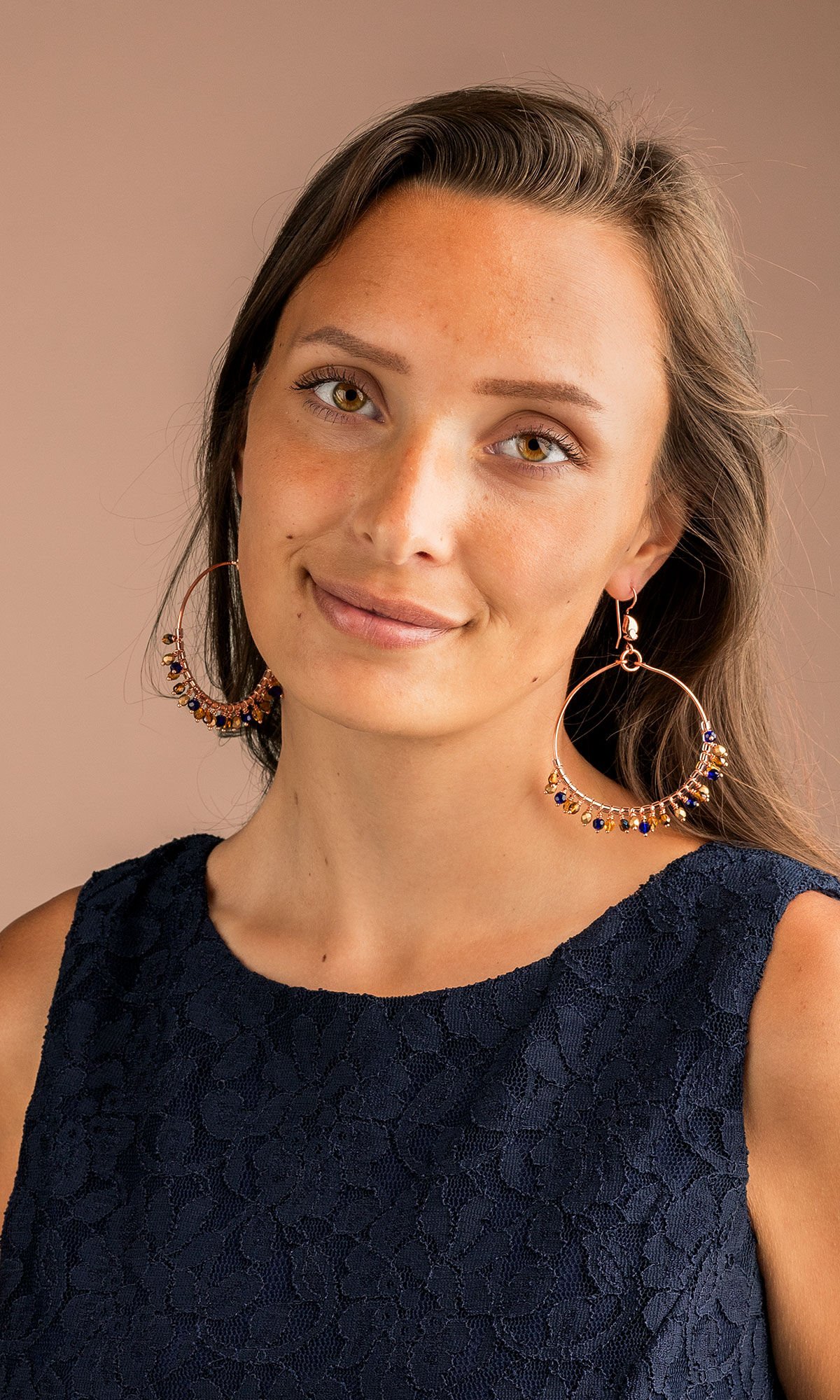 Model wearing design idea R H 2 8 Earrings with large circles of wire, and each circle has 24 small beaded drops in a pattern of blue and gold hues.