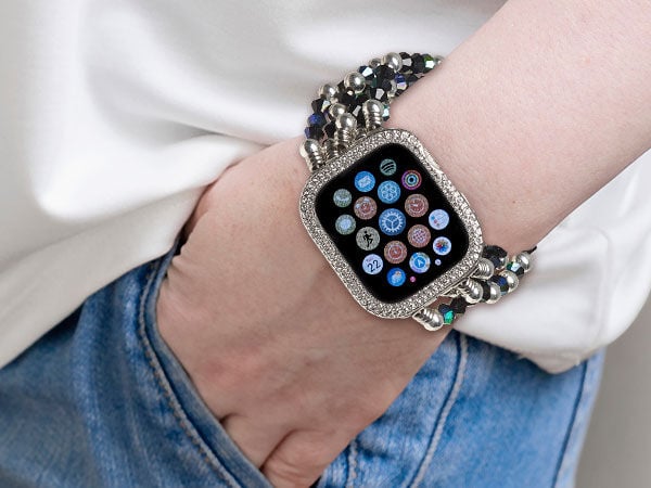 A person wearing a silver watch styled with a glittering rhinestones and a multi-strand beaded metallic bracelet band.